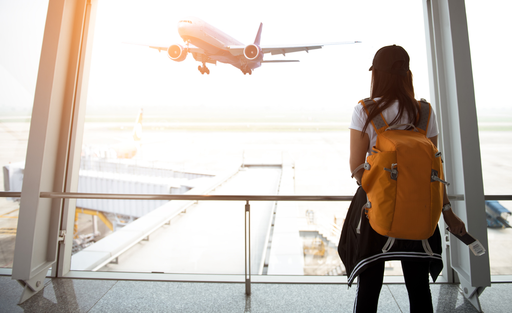 Illustration: eine junge Frau mit Rucksack steht am Flughafen und beobachtet ein abhebendes Flugzeug
